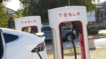 Dos estaciones de carga para vehículos eléctricos Tesla, con un coche blanco estacionado cerca.
