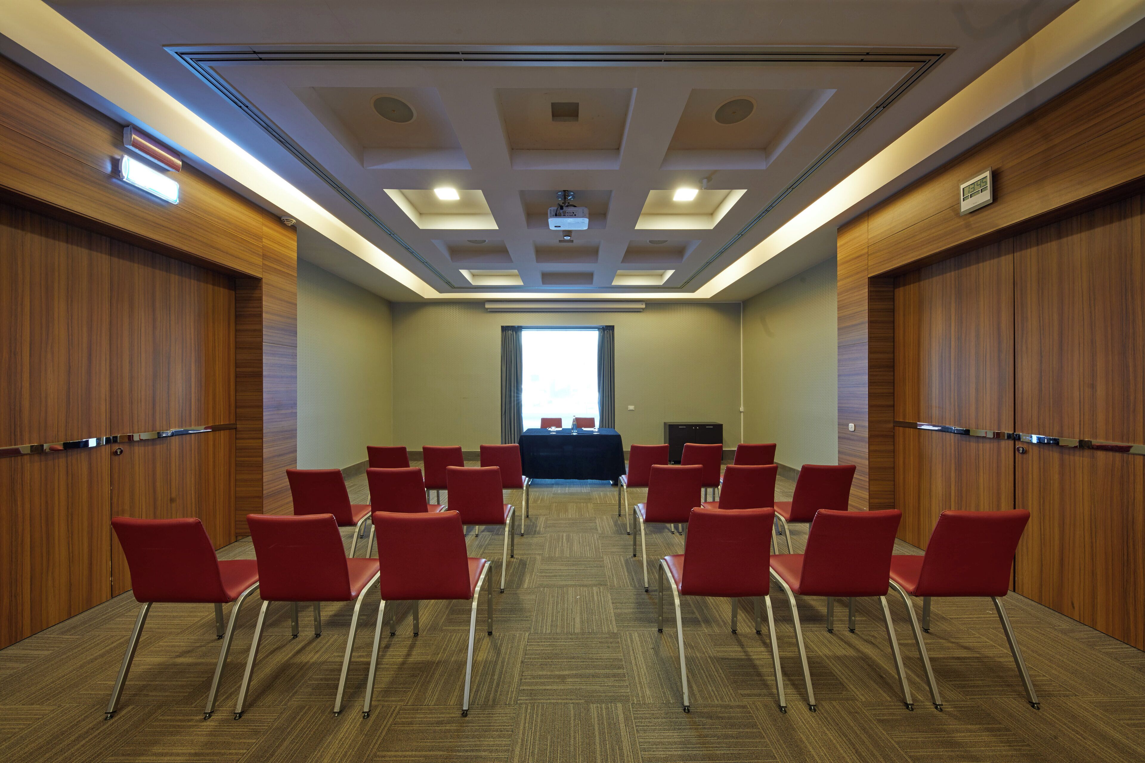 A conference room with a long table, red chairs, and a projector screen.