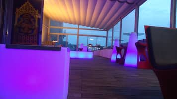 An outdoor seating area with tables and chairs, a large window, and a ceiling with a wave-like design.