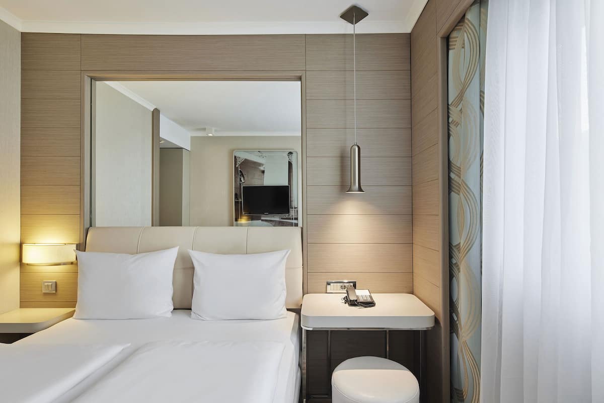 Quarto de hotel moderno com cama, mesa de cabeceira e um pequeno banheiro.