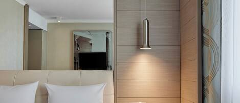 A modern hotel room with a large bed, a bedside table, a mirror, and a hanging pendant light.