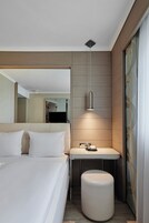 A modern hotel room with a large bed, a bedside table, a mirror, and a hanging pendant light.