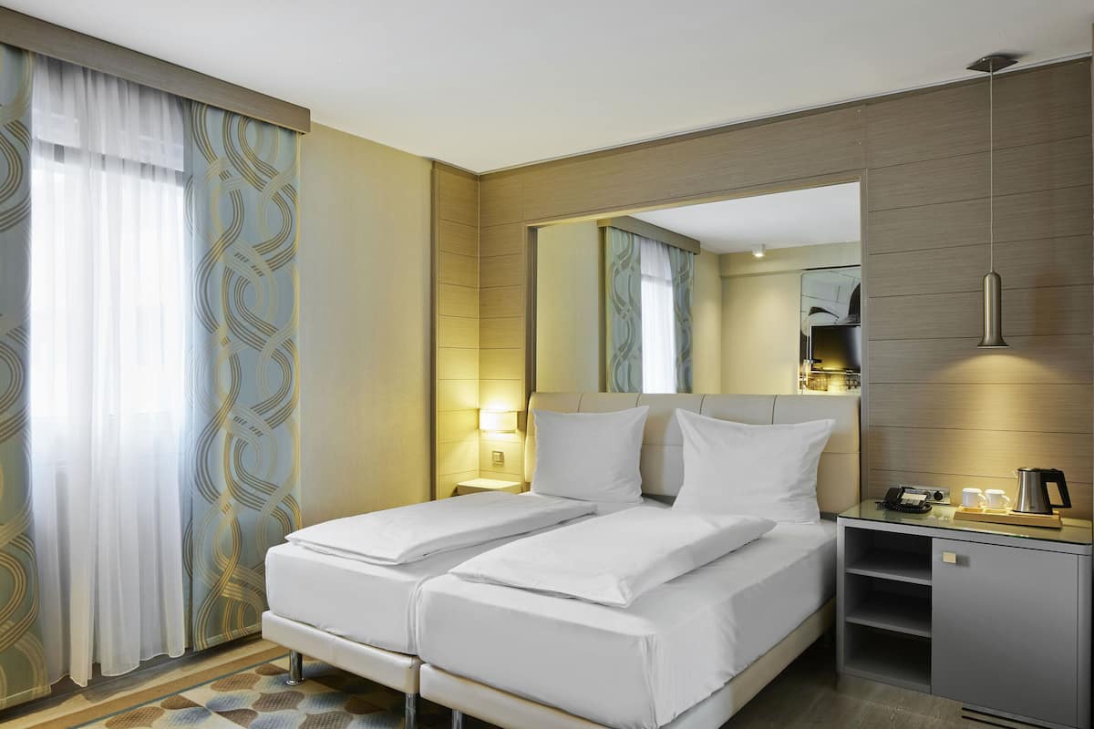 Quarto de hotel com cama de casal, mesa de cabeceira com abajur, espelho e um pequeno armário.
