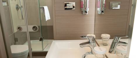 A modern bathroom with a glass shower enclosure, a white sink with dual faucets, and a mirror reflecting the room.