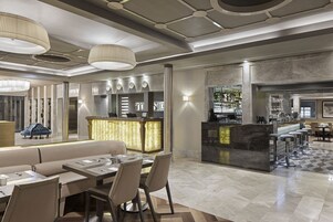 A modern hotel lobby with a bar area, seating arrangements, and a check-in desk.