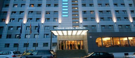 The exterior of the Titanic Hotel Berlin with a modern facade, multiple windows, and a prominent entrance with steps leading up to the lobby.