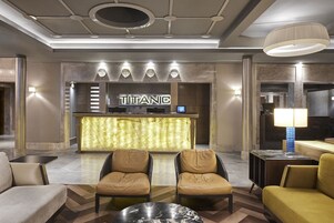 A lobby with a reception desk labeled "TITANIC," leather chairs, a marble coffee table, and a modern ceiling design.