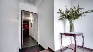 A hallway with a red carpet leading to a room, a vase with flowers on a table, and a door with a sign.