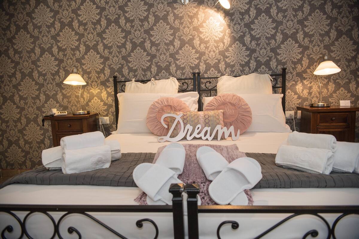 Cama bem arrumada com um letreiro 'Dream', duas luminárias laterais e papel de parede estampado.