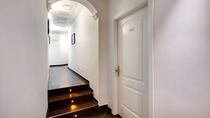 A hallway with a white door, a framed picture on the wall, and a staircase leading to another room.