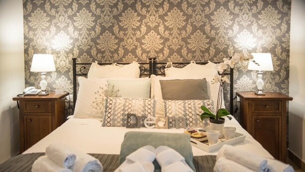 A neatly made bed with pillows, a bedside table with a lamp, a tray with a plant, and rolled towels on the bed.