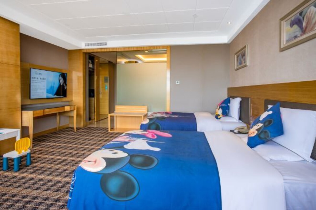 Habitación de hotel con dos camas, televisión, escritorio y una silla.