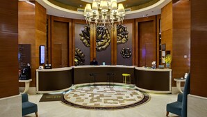 A hotel lobby with a reception desk, two bar stools, a chandelier, and a decorative wall piece. - Grand Skylight International Hotel Nanchang (Nanchang)