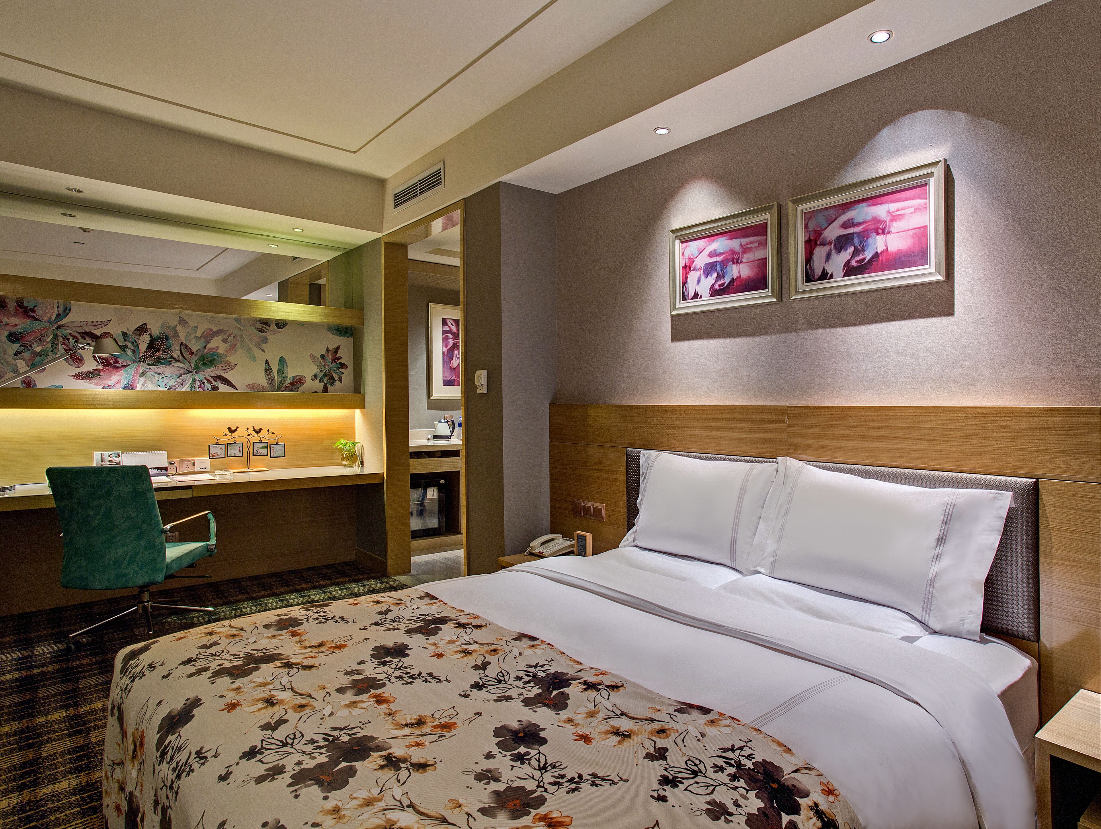 Quarto de hotel com cama, escrivaninha e duas molduras na parede.