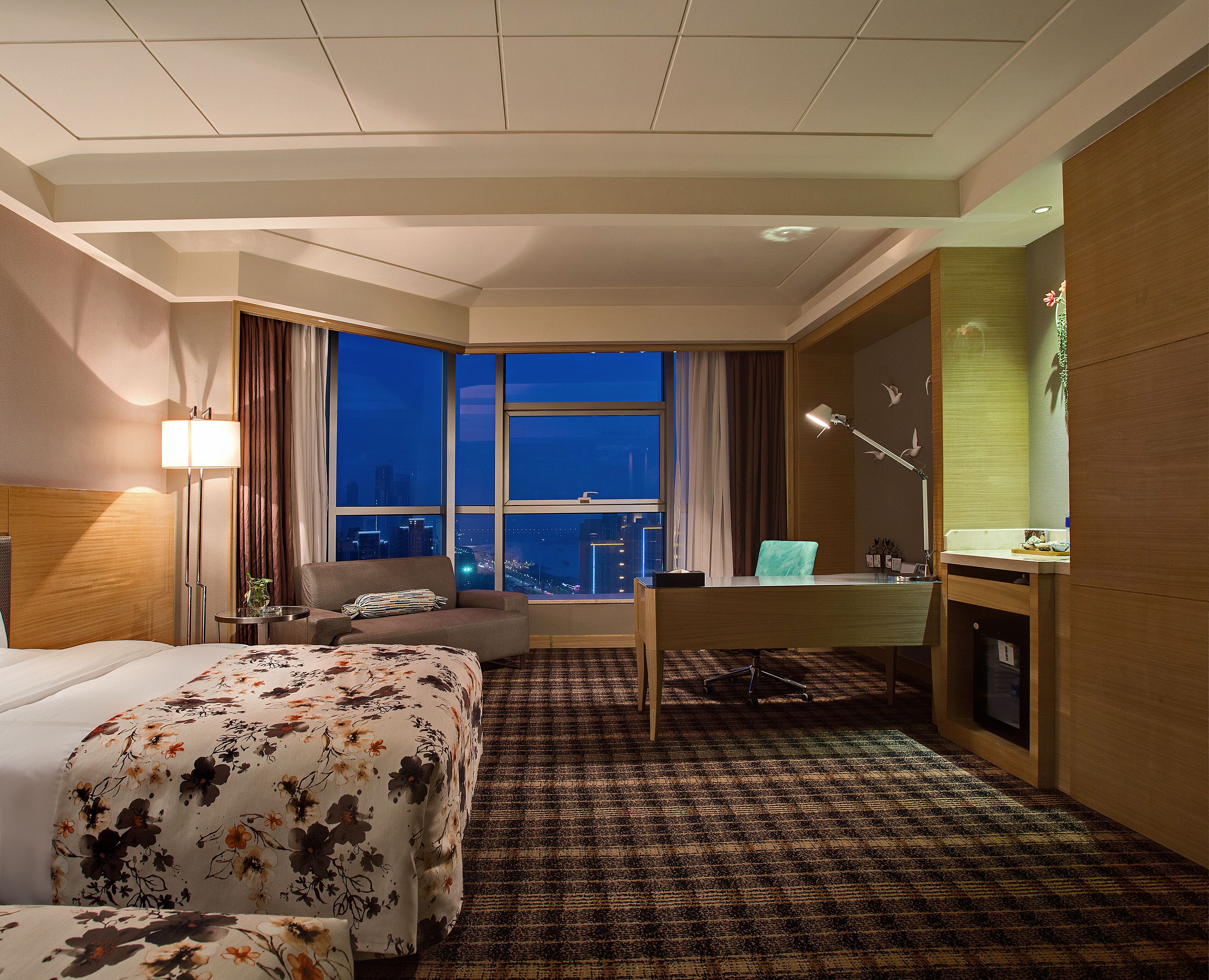 Una habitación de hotel con un ventanal grande, un escritorio, una silla, una cama y un baño.