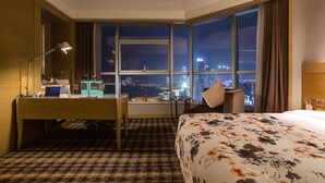 A hotel room with a desk, a bed, a chair, and a large window offering a city view at night. - Grand Skylight International Hotel Nanchang (Nanchang)