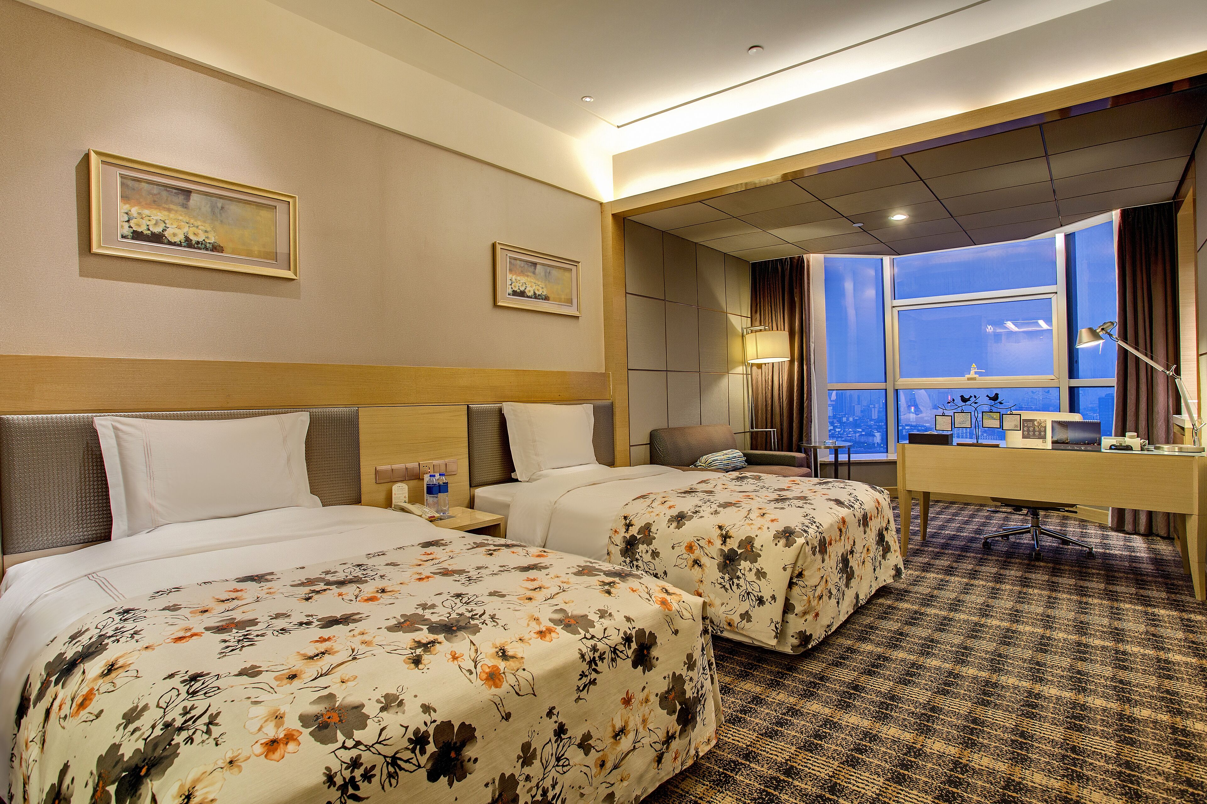 A hotel room with two beds, a desk, a chair, and a large window with a view.
