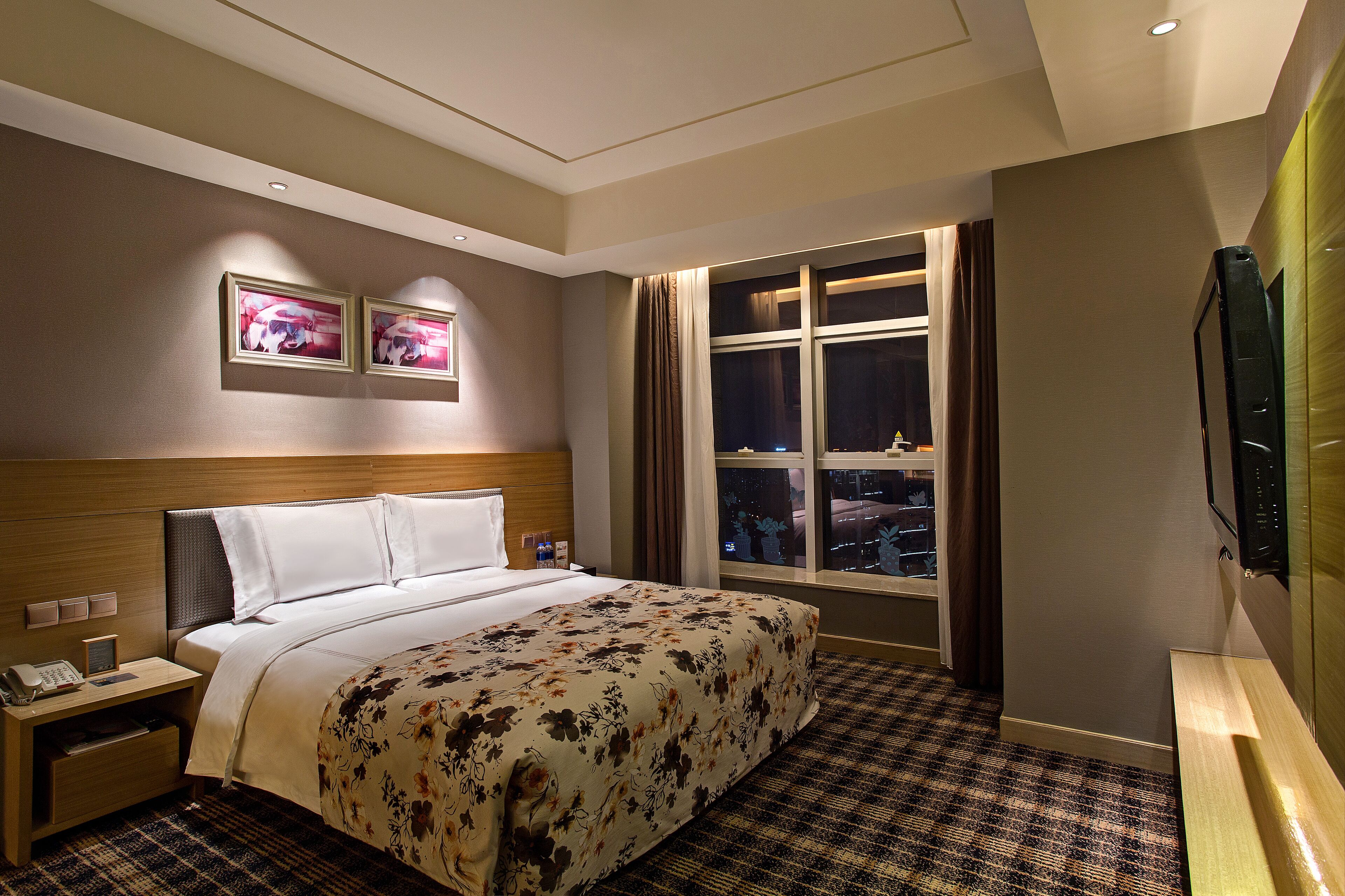 A hotel room with a bed, bedside tables, a TV, and a window with curtains.