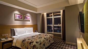 A hotel room with a bed, bedside tables, a TV, and a window with curtains.