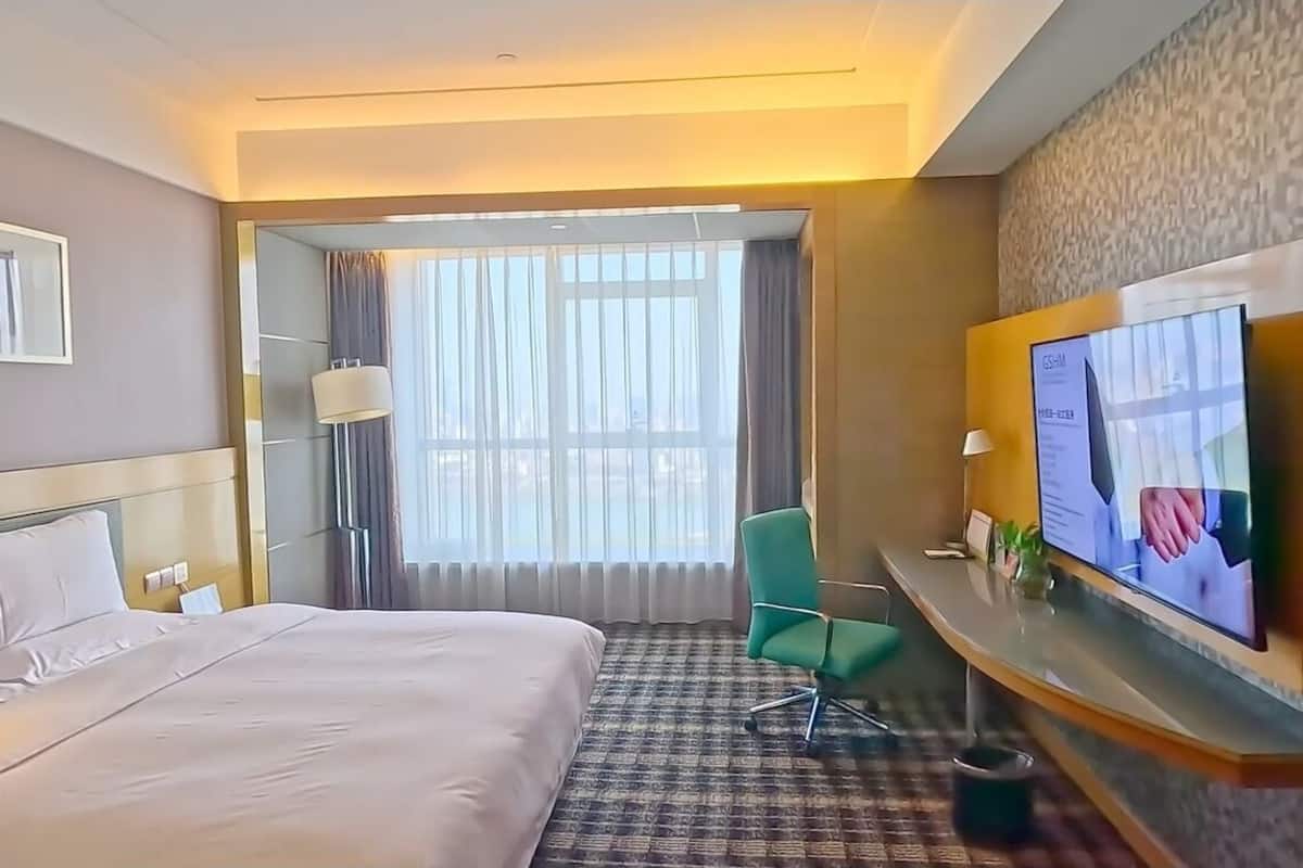 Une chambre d’hôtel avec un lit, un bureau avec une télévision, une chaise et une fenêtre avec des rideaux.