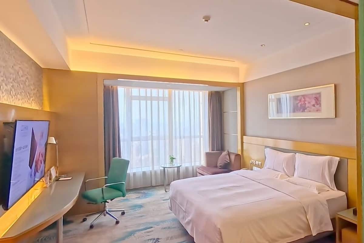 Une chambre d’hôtel avec un lit, un bureau, une chaise, une télévision et une fenêtre avec des rideaux.