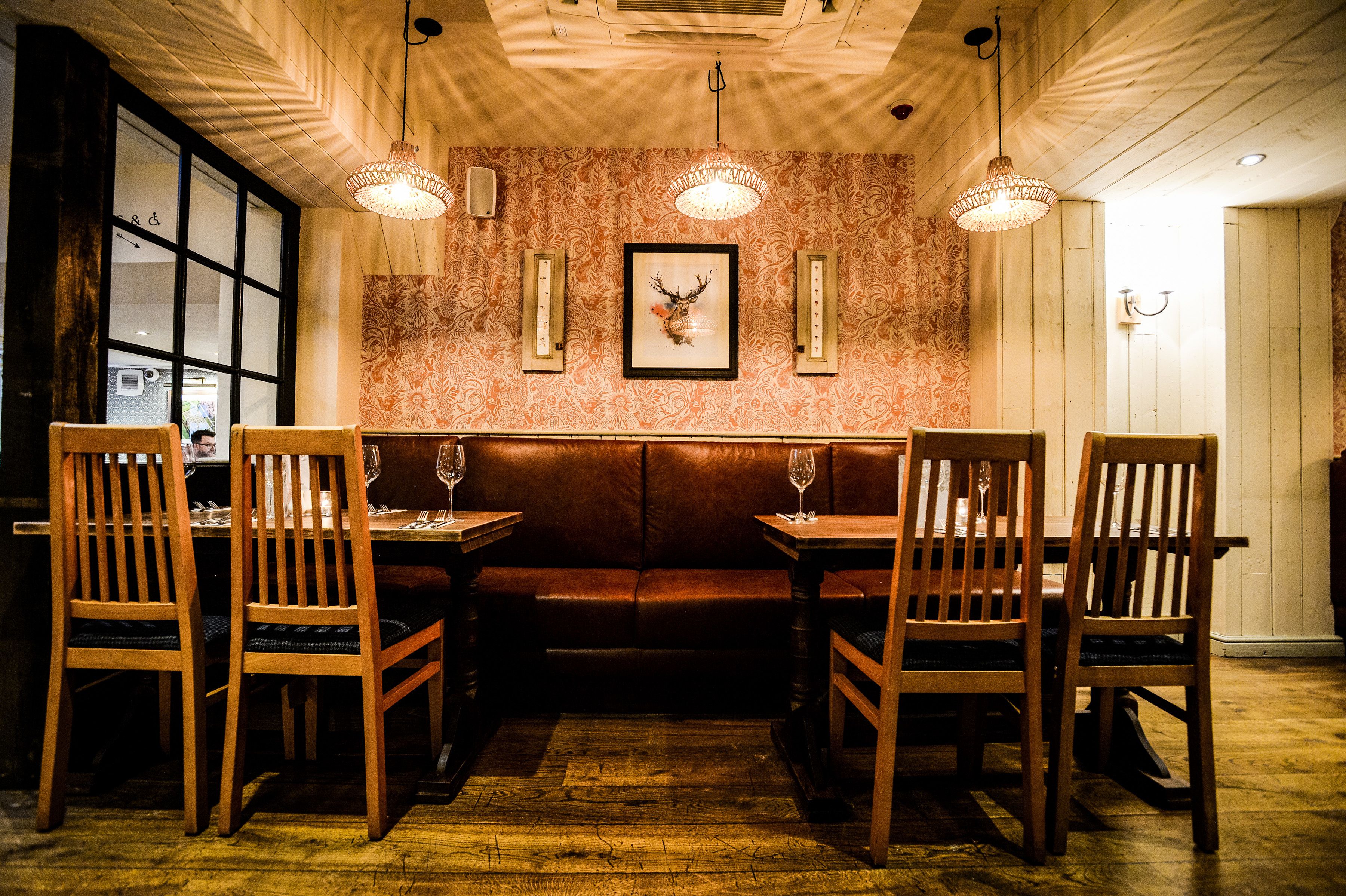 Un restaurante con mobiliario de madera, un papel tapiz estampado y un cuadro de un ciervo enmarcado.