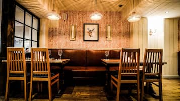 Un restaurante con mobiliario de madera, un papel tapiz estampado y un cuadro de un ciervo enmarcado.