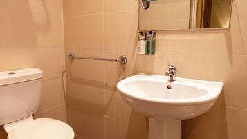 Een badkamer met toilet, een witte wastafel, een glazen plank en een spiegel.