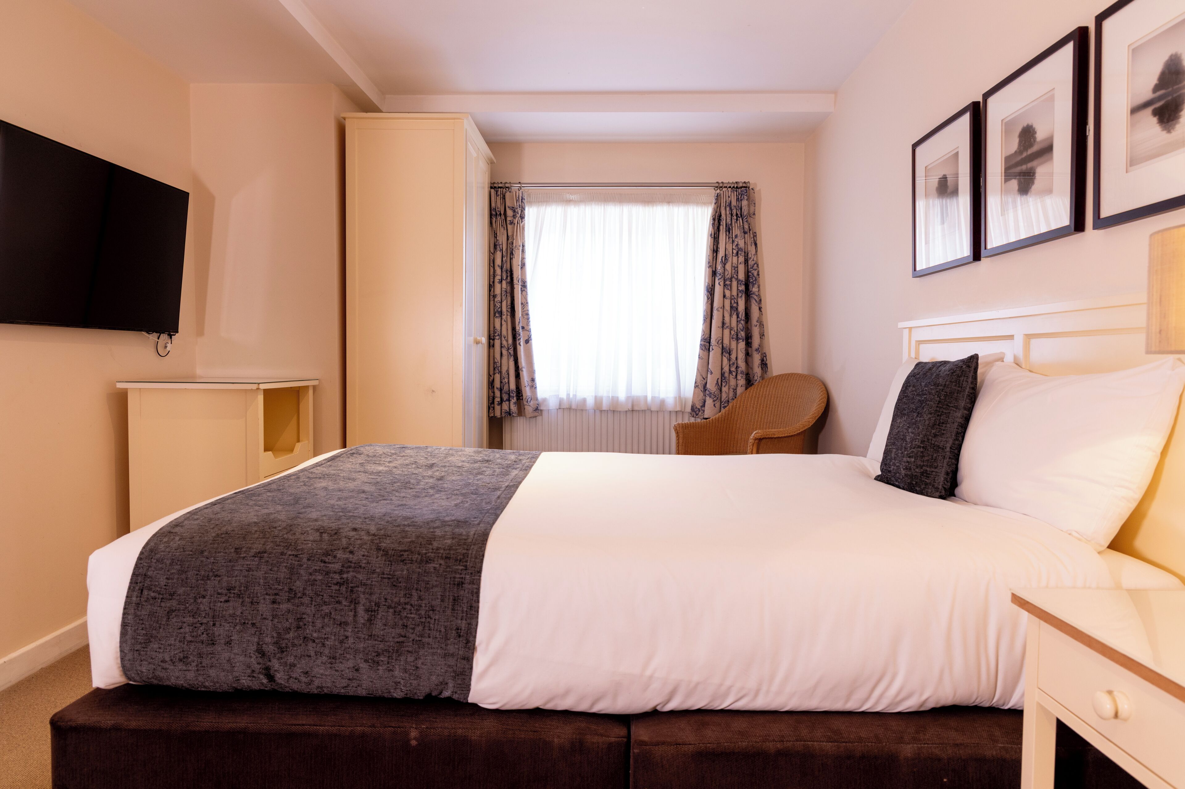 A hotel room with a bed, a TV mounted on the wall, a wardrobe, and a window with curtains.