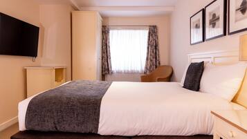 A hotel room with a bed, a TV mounted on the wall, a wardrobe, and a window with curtains.
