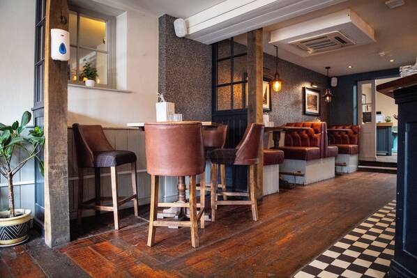 Una zona de bar con taburetes de madera y asientos acolchados, suelo a cuadros y un ventanal con vistas.