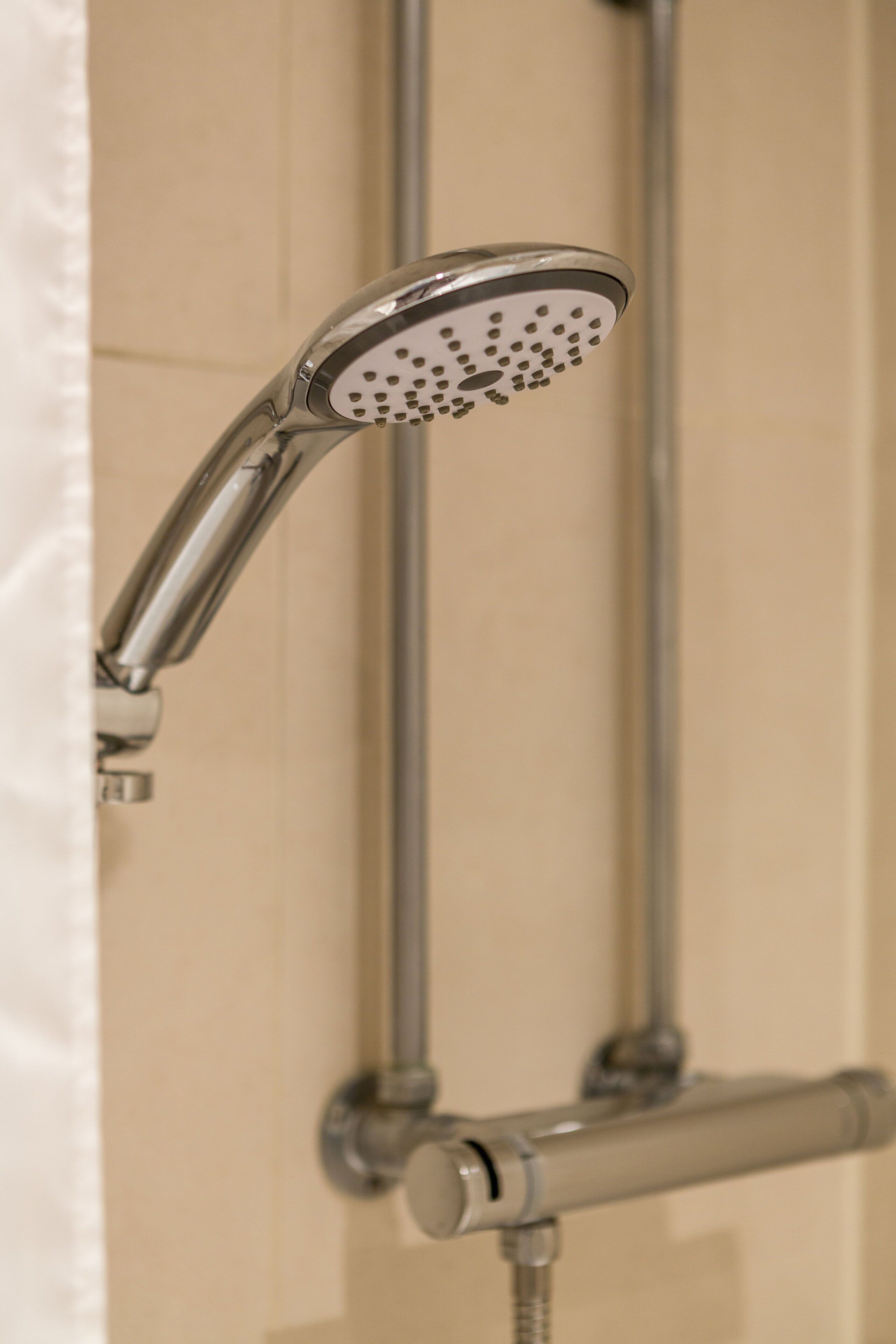 A showerhead with multiple nozzles, a handheld shower attachment, and a vertical pipe, likely part of a bathroom's shower system.
