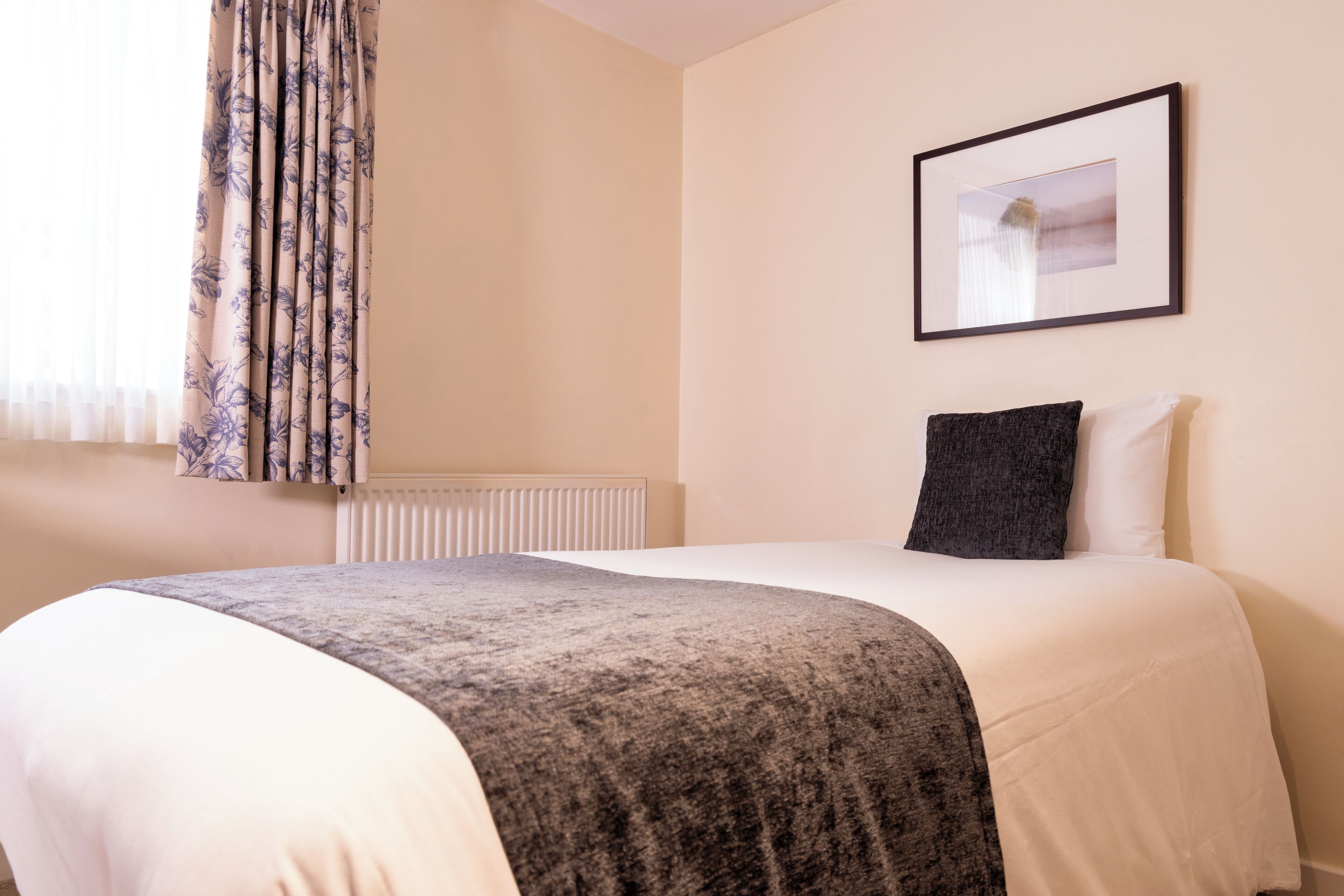 A hotel room with a bed, a framed picture on the wall, and a window with curtains.