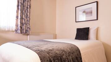 A hotel room with a bed, a framed picture on the wall, and a window with curtains.