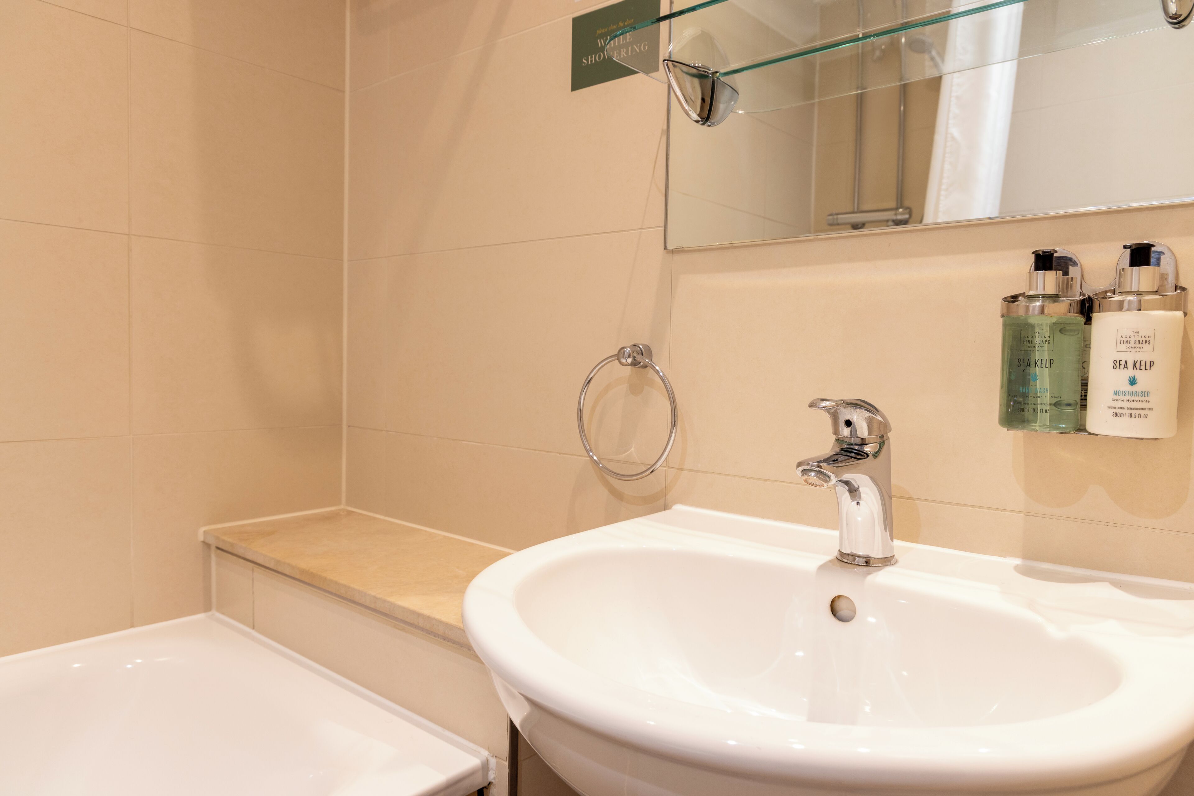 Un baño con un lavamanos blanco, cabina de ducha con mampara de vidrio y artículos de aseo en la pared.
