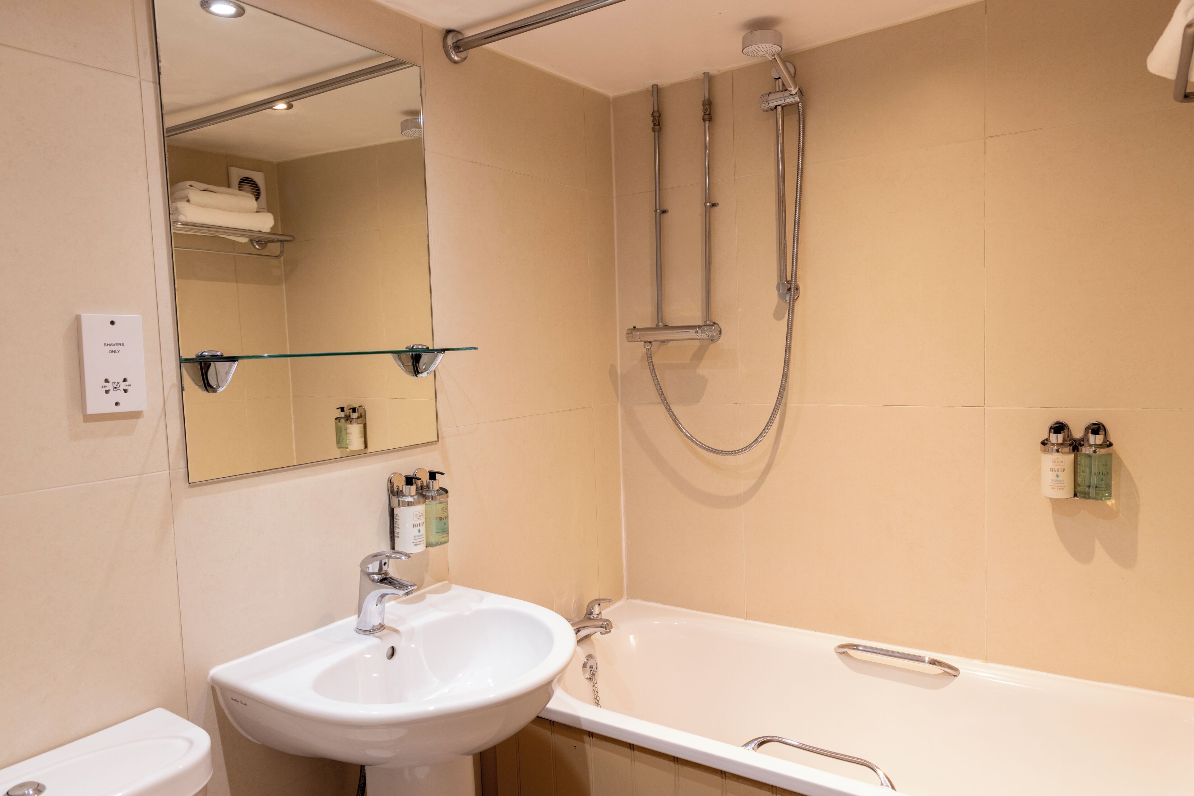 Un baño con lavamanos, espejo, ducha y toallero.