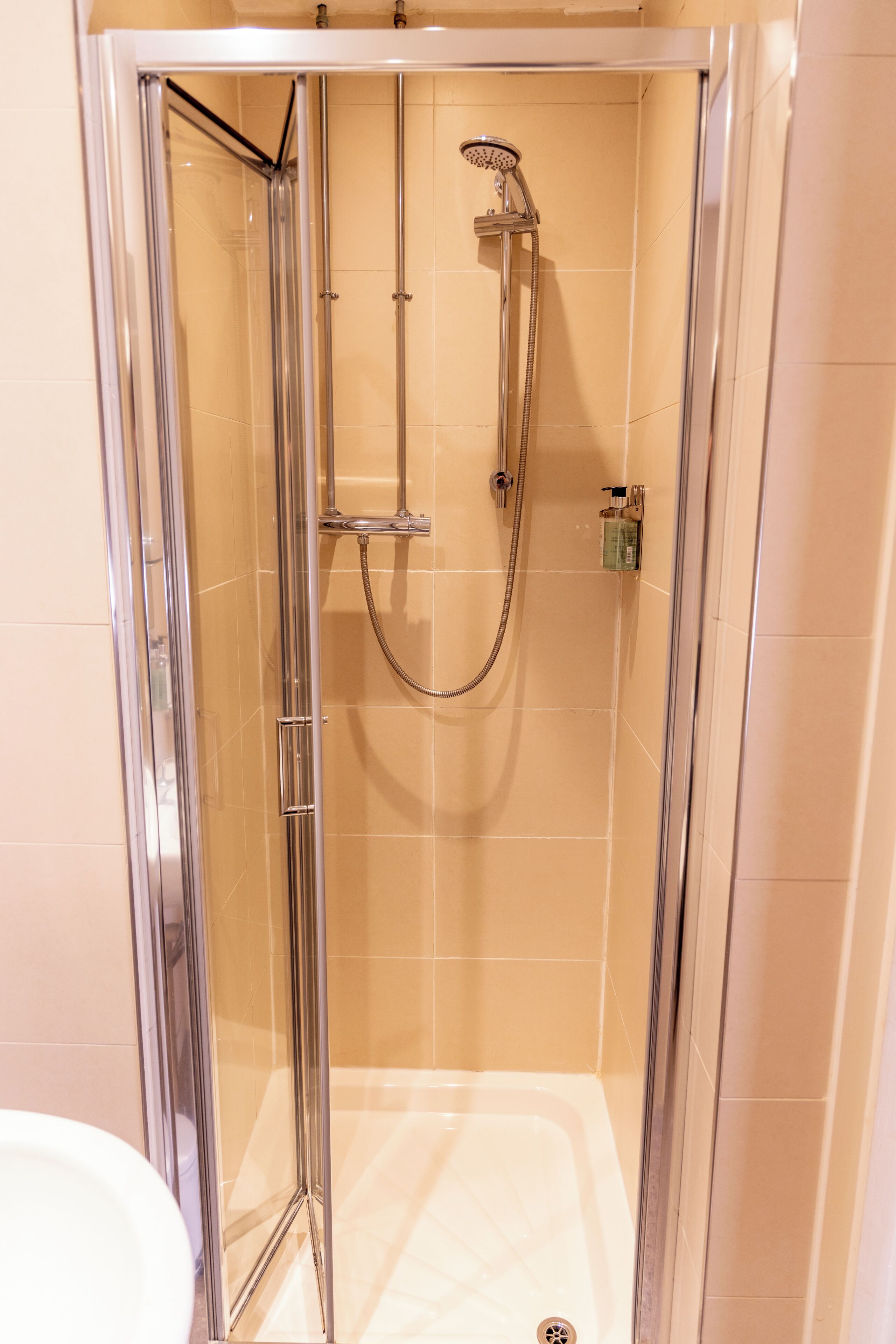 A glass-enclosed shower stall with a handheld showerhead and a wall-mounted faucet.
