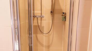 A glass-enclosed shower stall with a handheld showerhead and a wall-mounted faucet.