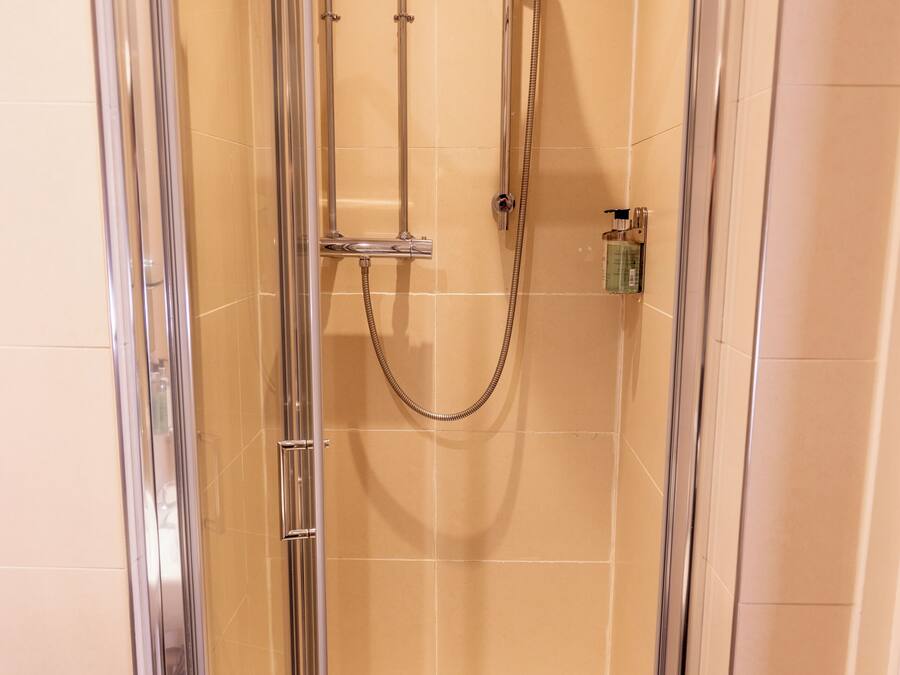 A glass-enclosed shower stall with a handheld showerhead and a wall-mounted faucet.
