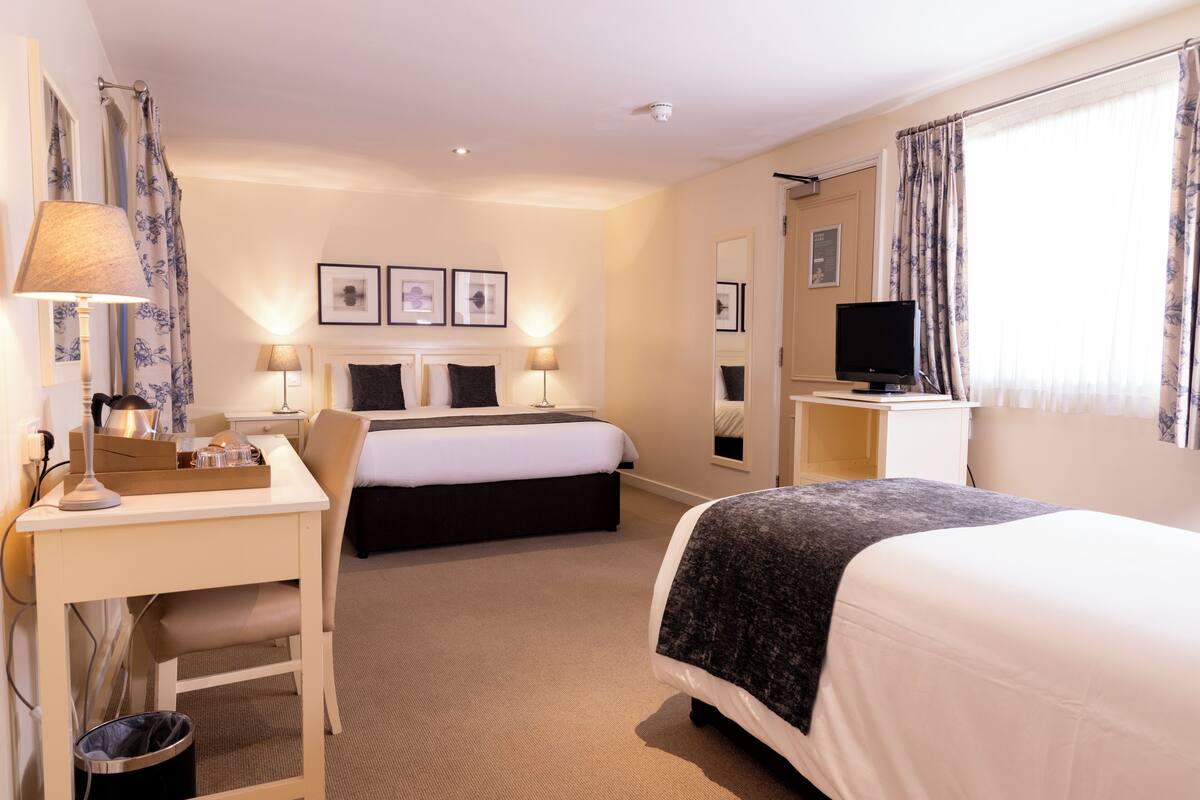 A hotel room with a bed, desk, chair, TV, and framed pictures on the wall.