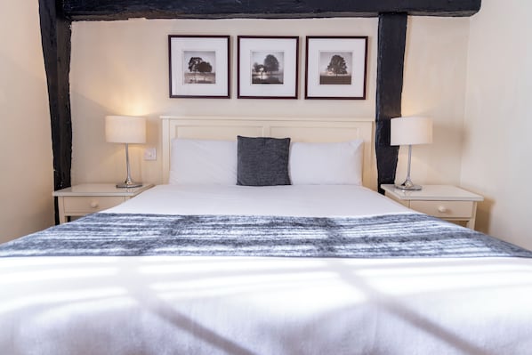 A neatly made bed with a striped blanket, two bedside lamps, a white headboard, and three framed pictures on the wall.
