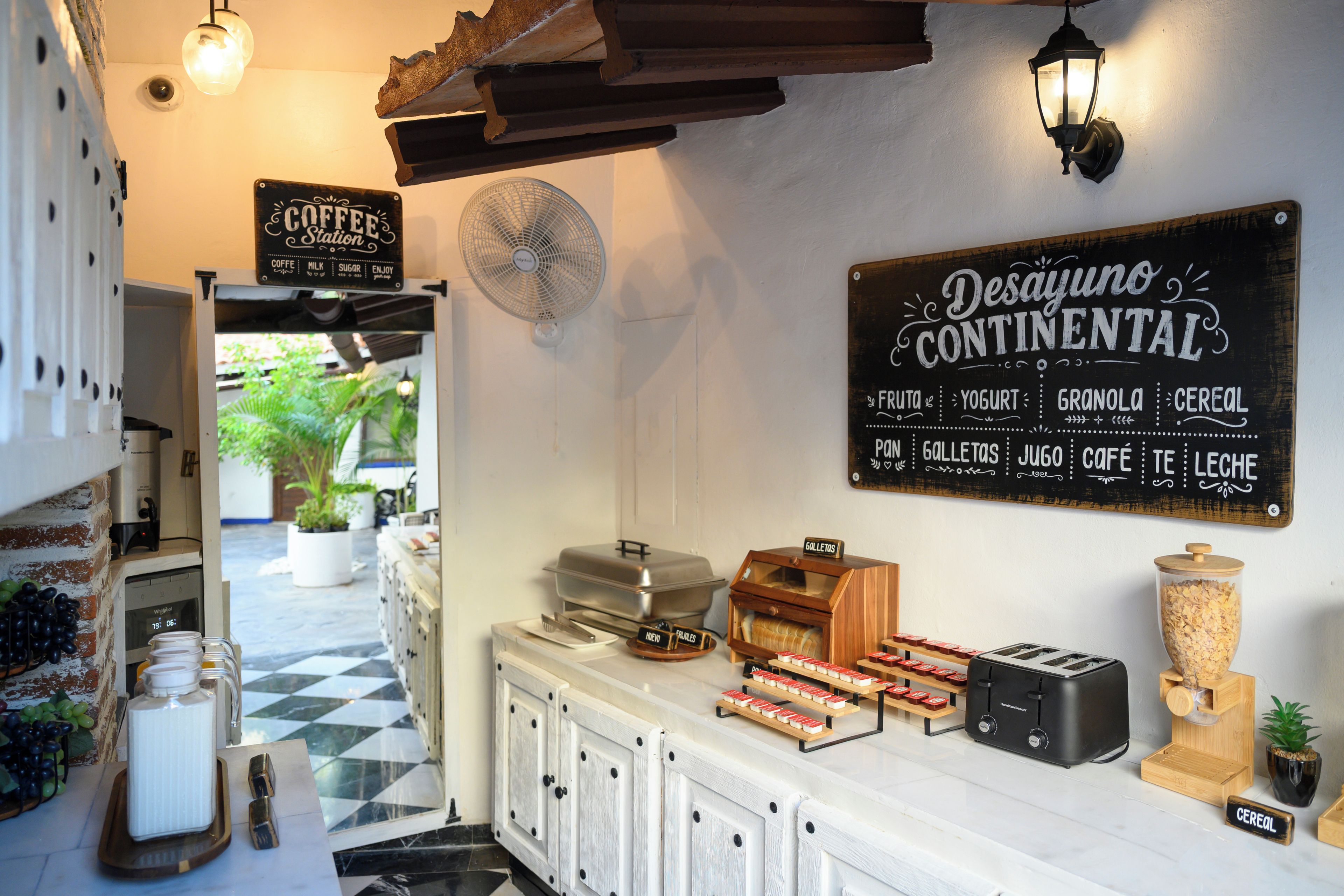 A café interior with a menu board, a fan, and various food items displayed.