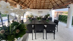 An outdoor patio with a thatched roof, a dining table with chairs, and white orchids. - Hotel Suites Mar Elena (Puerto Vallarta)