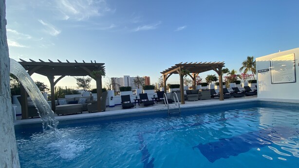 A pool area with lounge chairs and a pergola, surrounded by a fence and palm trees. - Hotel Suites Mar Elena (Puerto Vallarta)