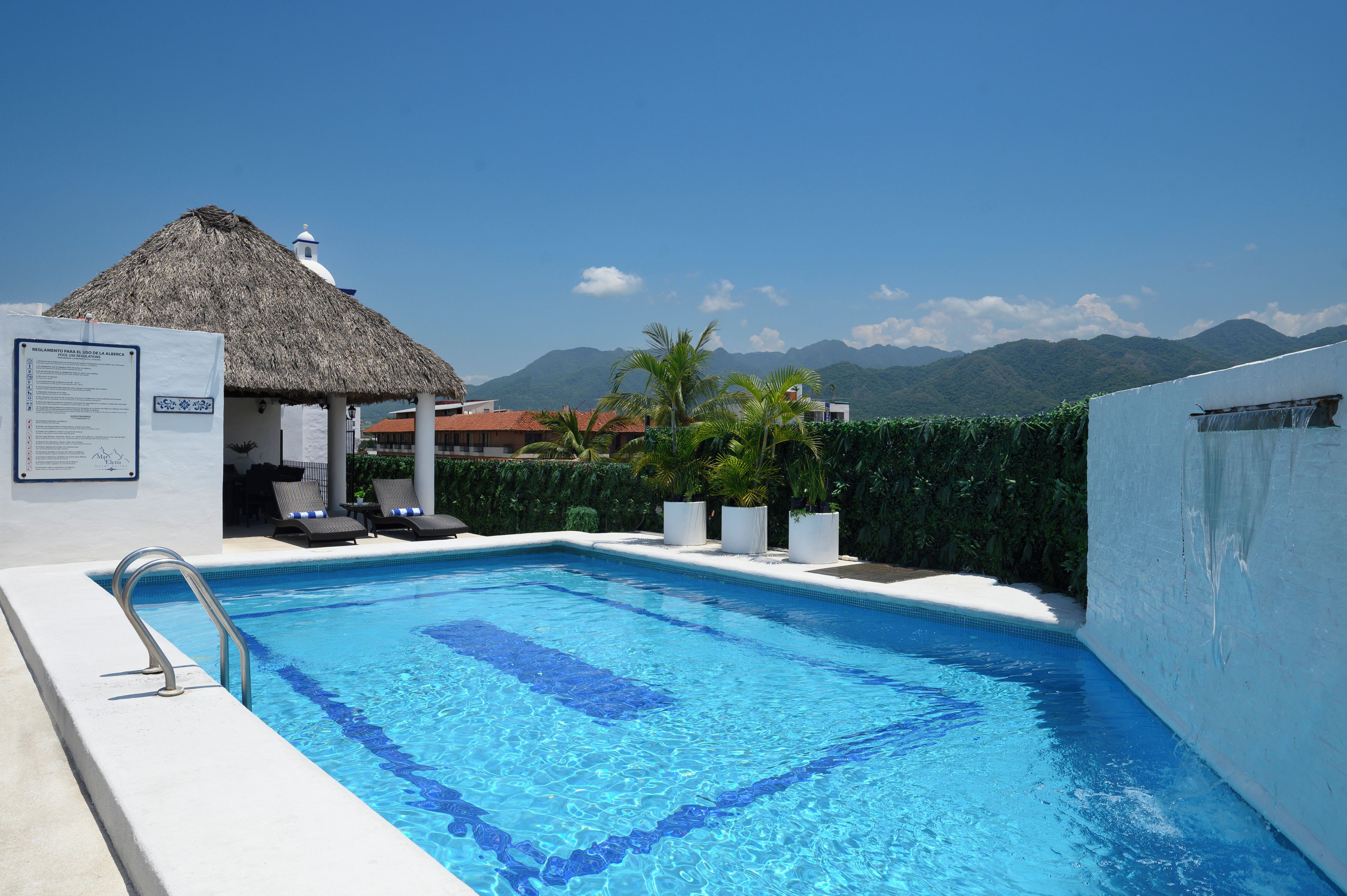 Une piscine avec un bassin aux eaux d’un bleu cristallin, une structure à toit de chaume et un paysage montagneux en arrière-plan.