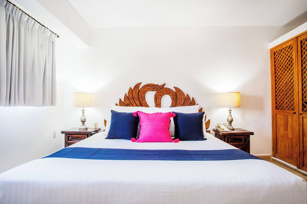 A hotel room with a large bed, two bedside tables with lamps, a wooden headboard, and a wardrobe.