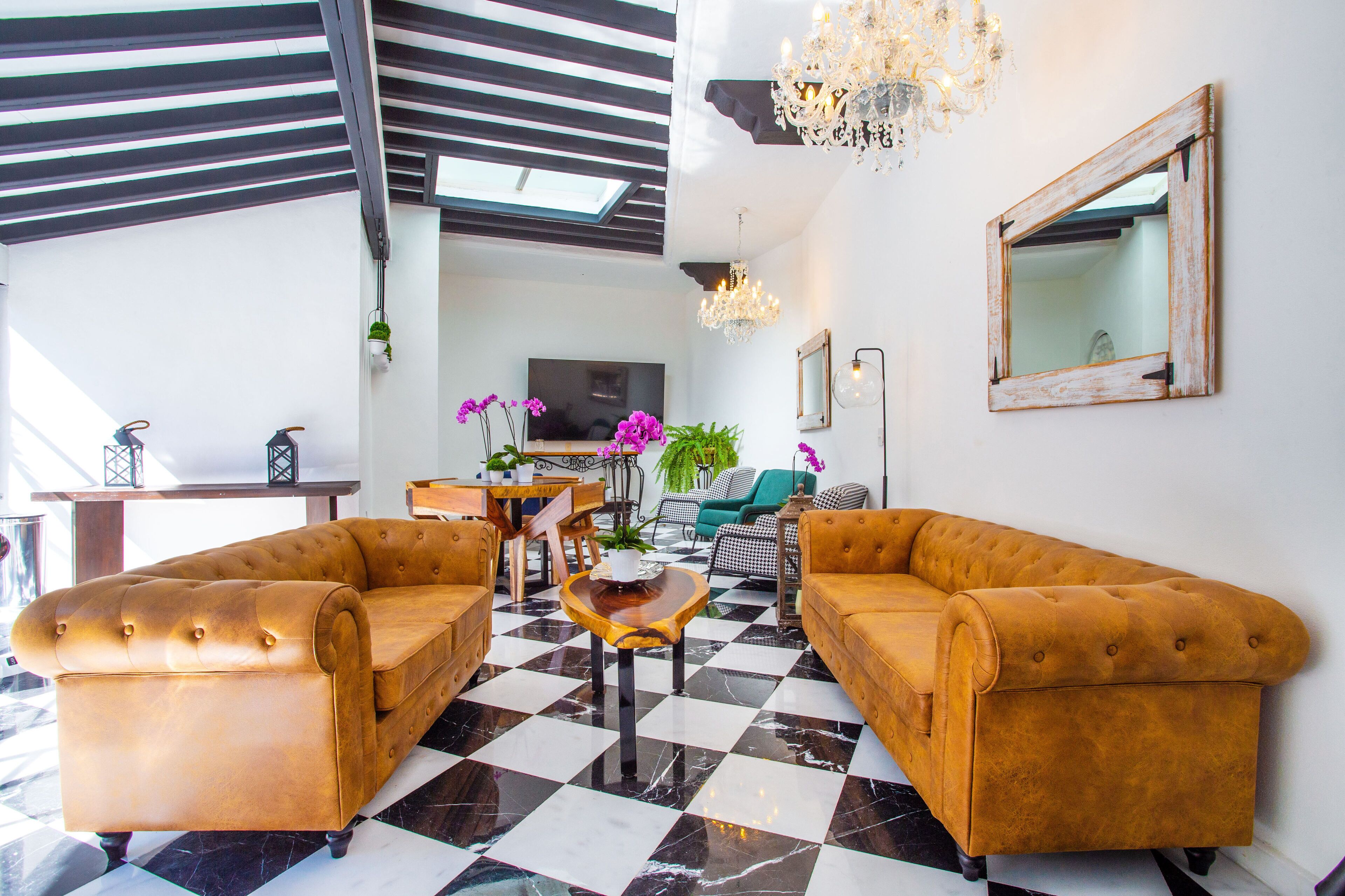 Un salon moderne avec un sol à carreaux, deux canapés en cuir, une table basse en bois et un lustre.