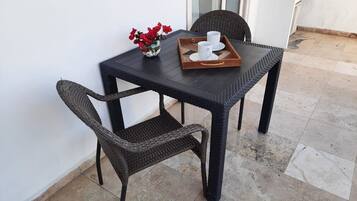 A small outdoor table with two wicker chairs, a tray with cups, and a vase with red flowers.