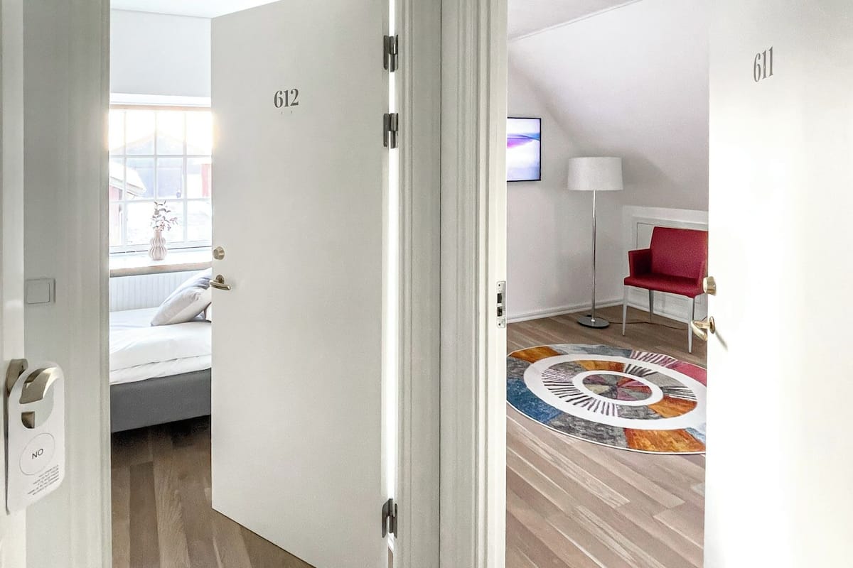Ein Hotelzimmer mit Holzboden, einem Bett mit Kissen, einem an der Wand befestigten Fernseher und einem roten Sessel.