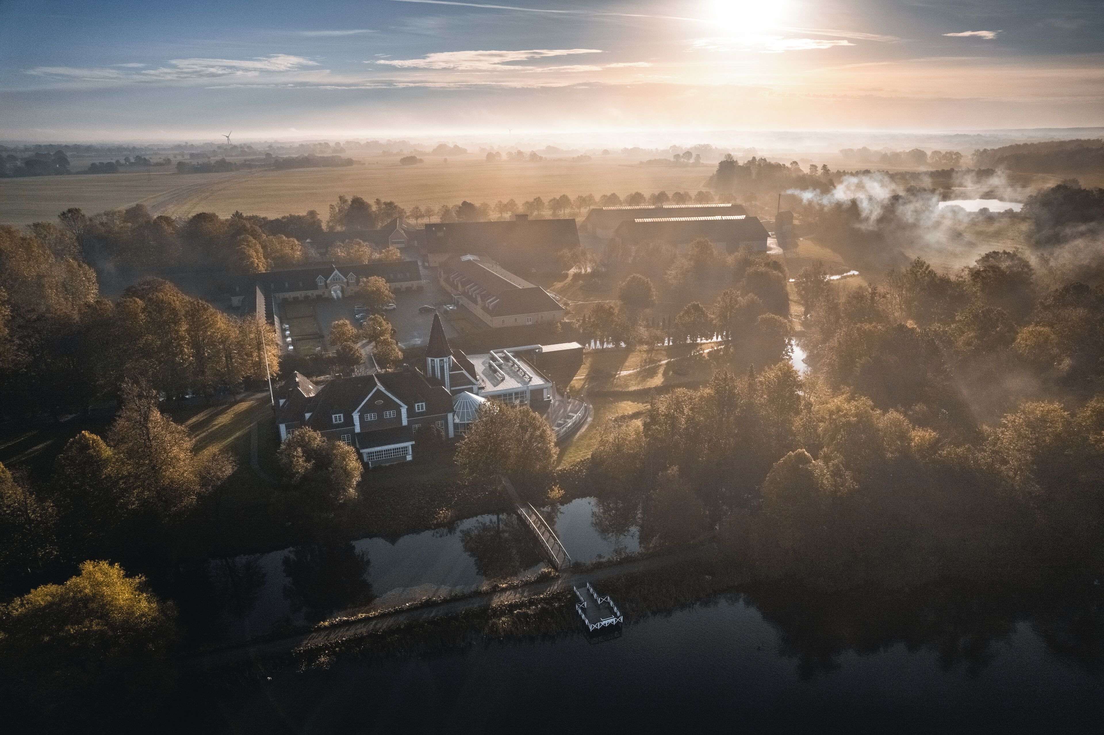 An aerial view of a rural estate with a large house, a barn, and a small body of water.